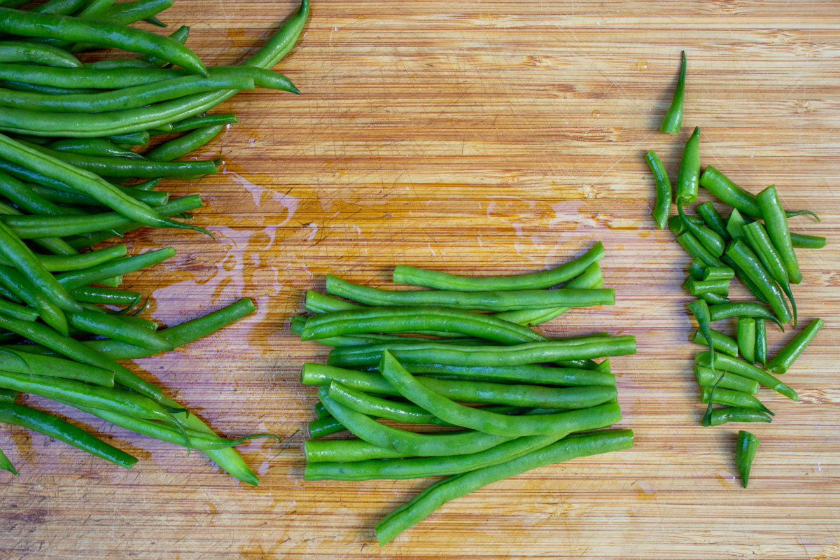 trimmed green beans on cutting board with trimmed ends on the side. 