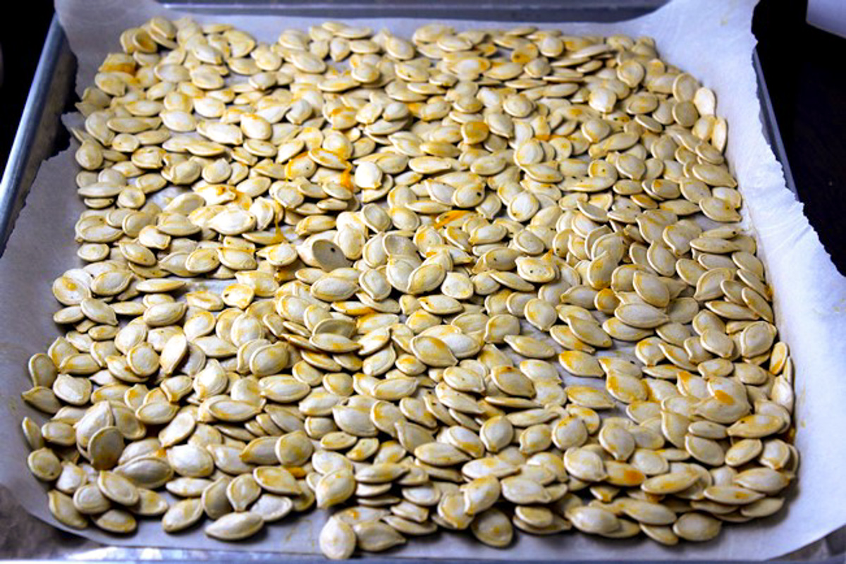 raw pumpkin seeds spread on baking sheet.