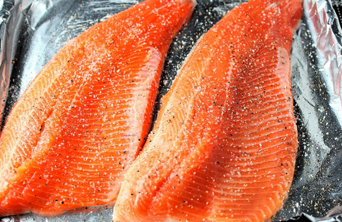 two raw trout fillets on pan with seasoning.