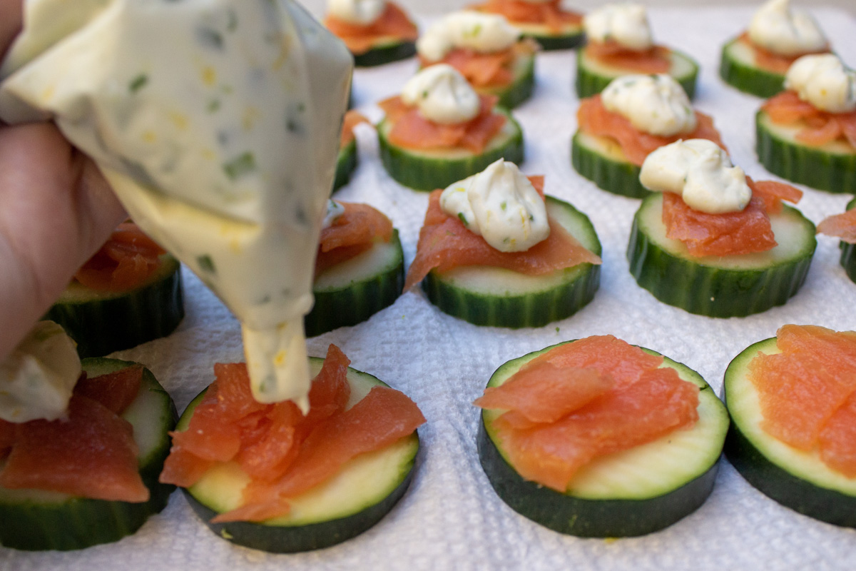 cream cheese being piped with bag onto zucchini rounds topped with smoked salmon.