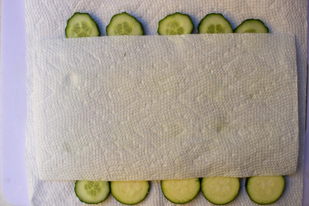 cucumbers and zucchini between paper towels on cutting board.