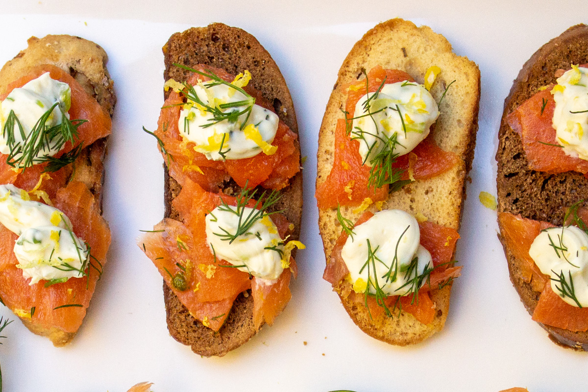 oblong bagel crackers topped with smoked salmon, cream cheese and dill on cutting board.