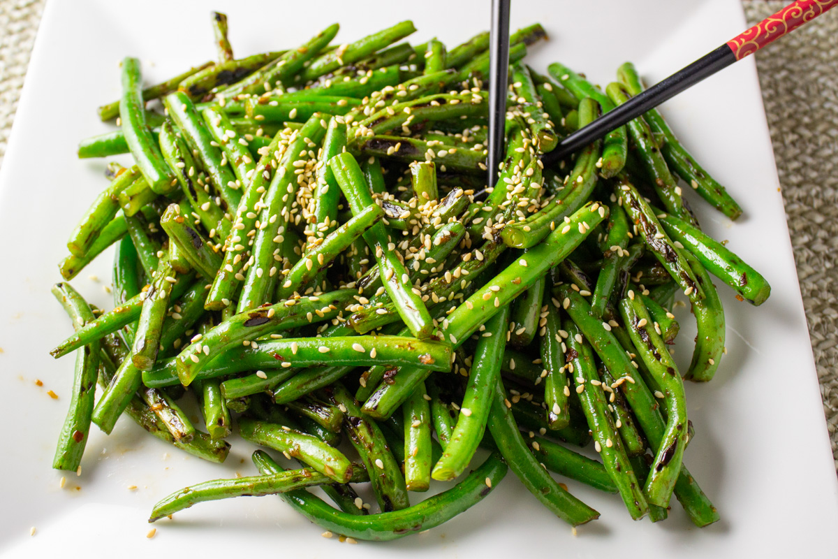 Chinese stir fry green beans topped with sesame seeds on plate with chopsticks.