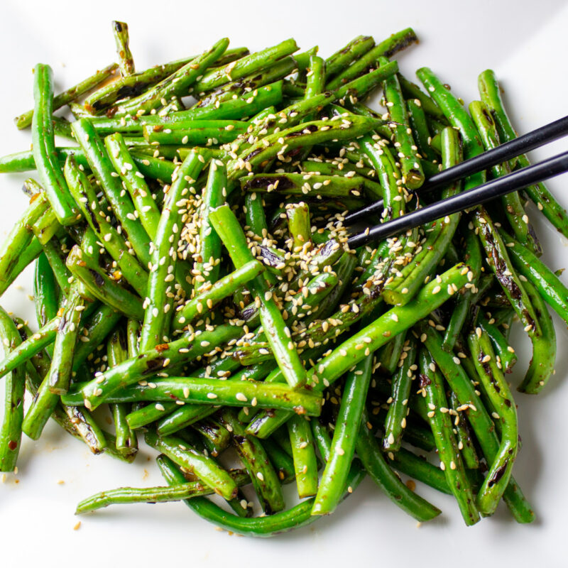 Chinese stir fry green beans topped with sesame seeds on plate with chopsticks.