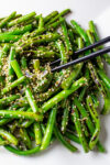 Chinese stir fry green beans topped with sesame seeds on plate with chopsticks.