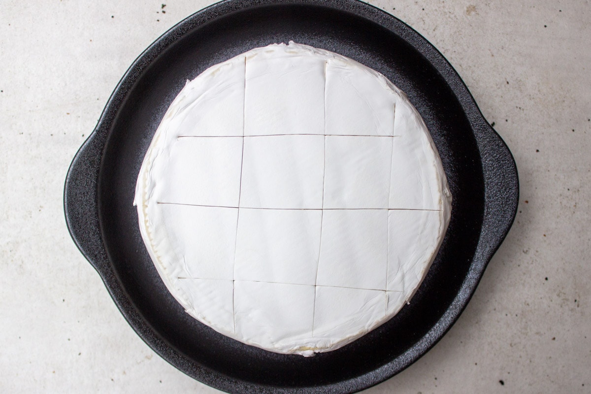 brie cheese wheel on plate with rind scored on top.