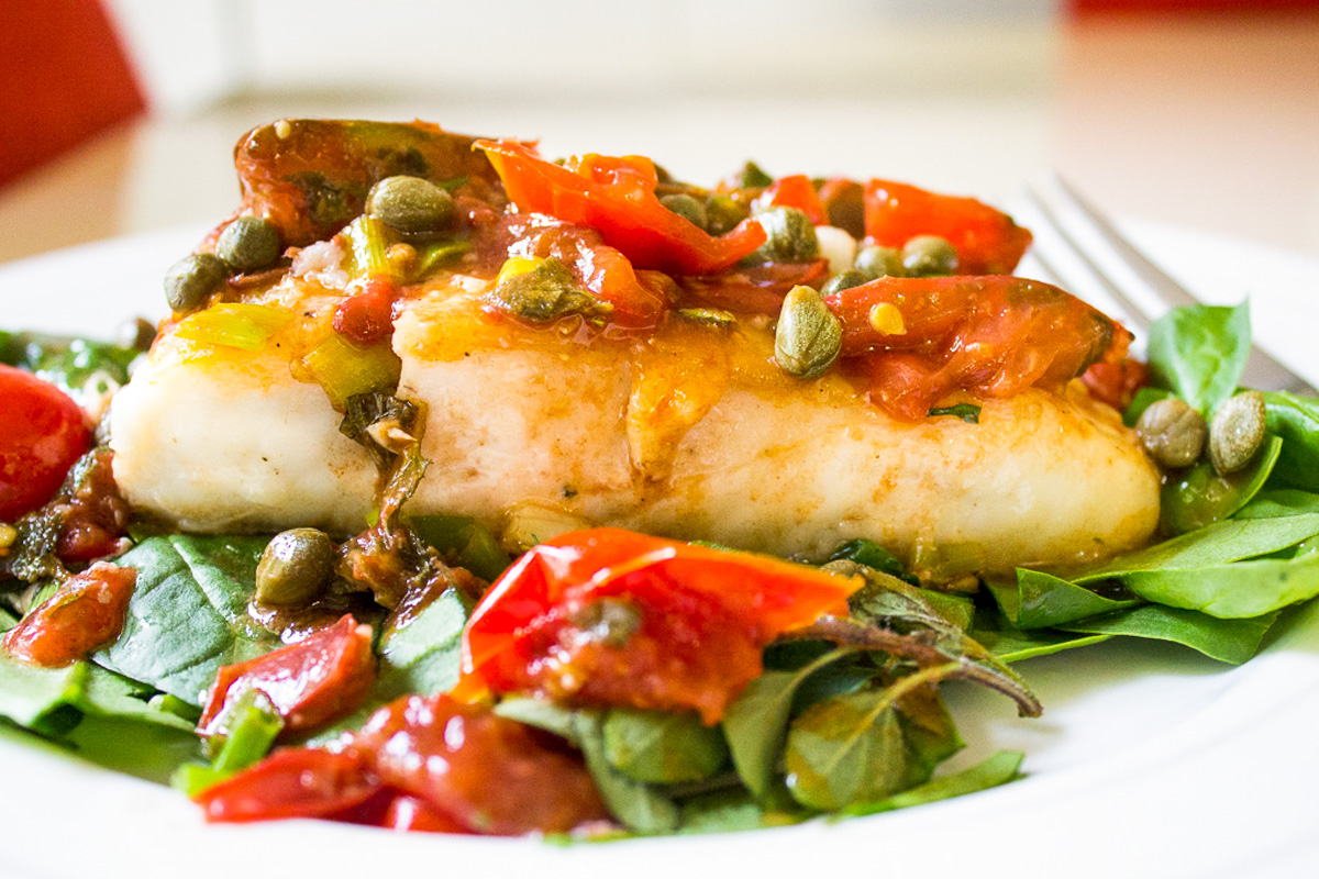 baked halibut with tomato caper herb sauce over spinach on plate.