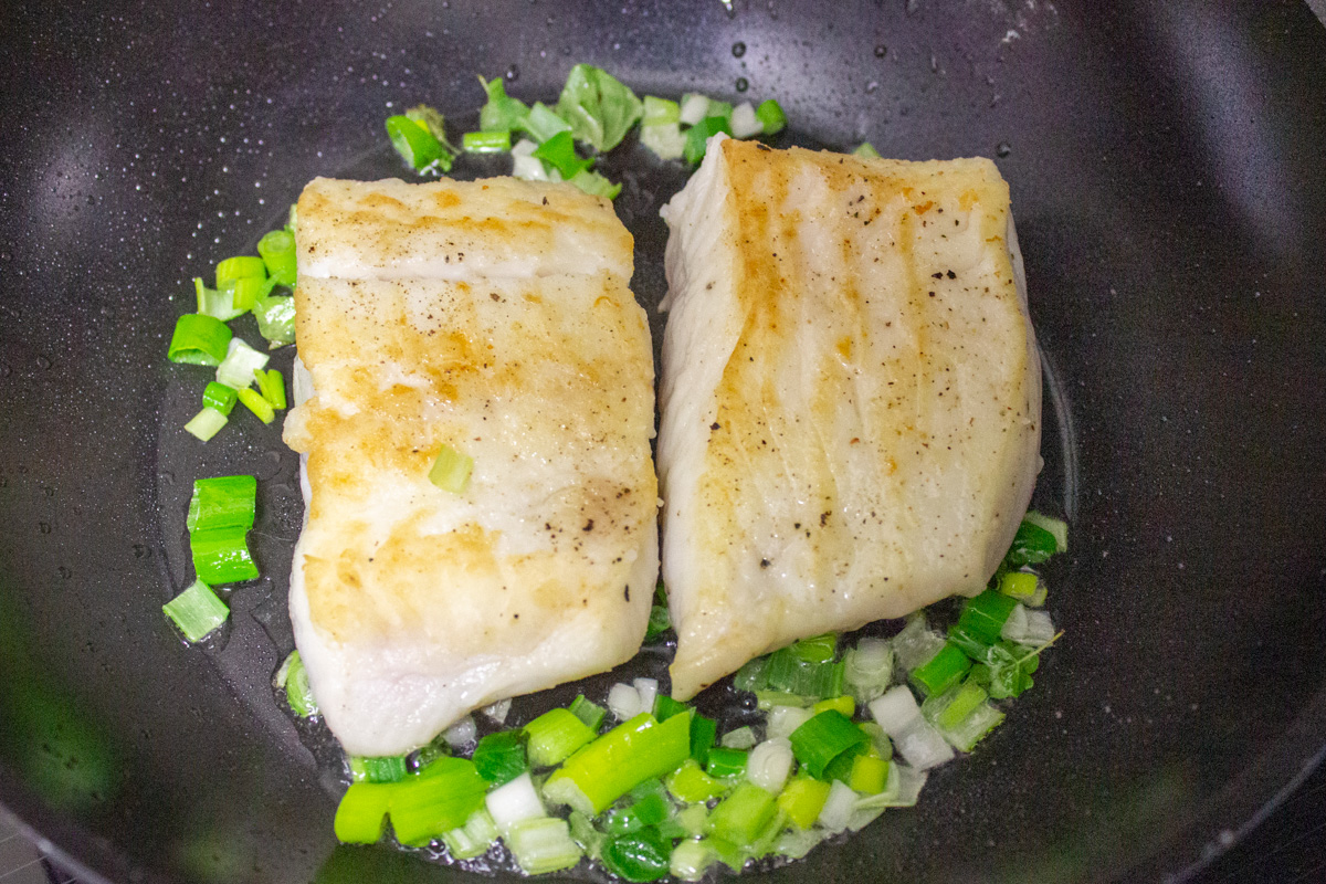 two pan seared halibut fillets with green onions in skillet.