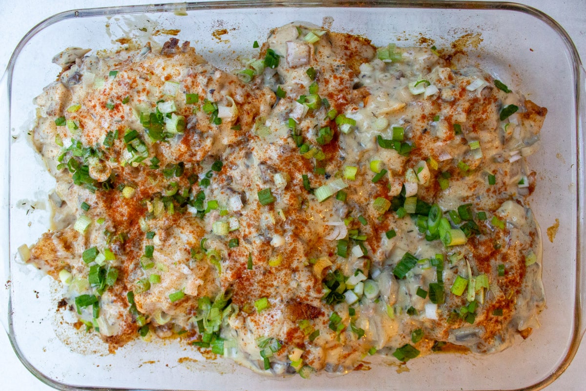 baked chicken with mushroom sauce, garnished with chopped green onions in pan.