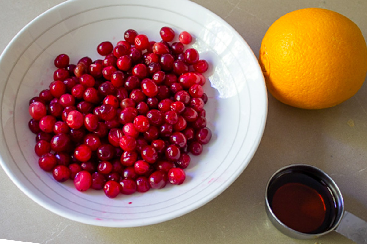bowl of fresh cranberries, one orange and maple syrup. 