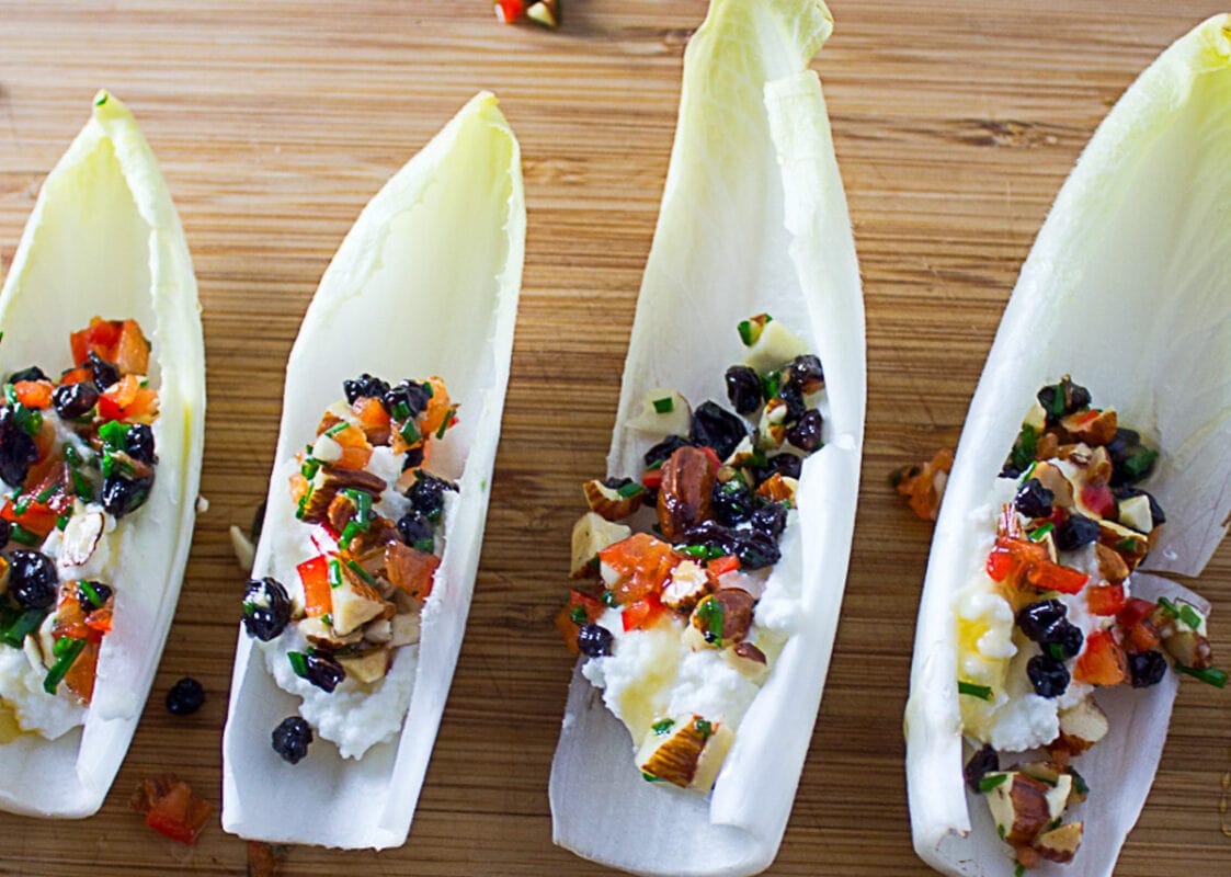 3 endive appetizers with ricotta, nuts, peppers and cranberries on cutting board