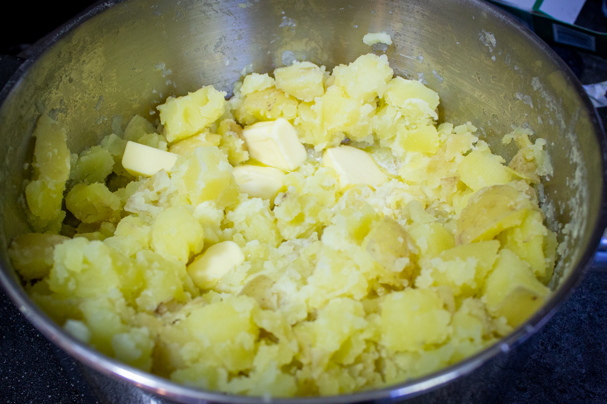 drained potatoes with butter and milk in pot not yet mashed.