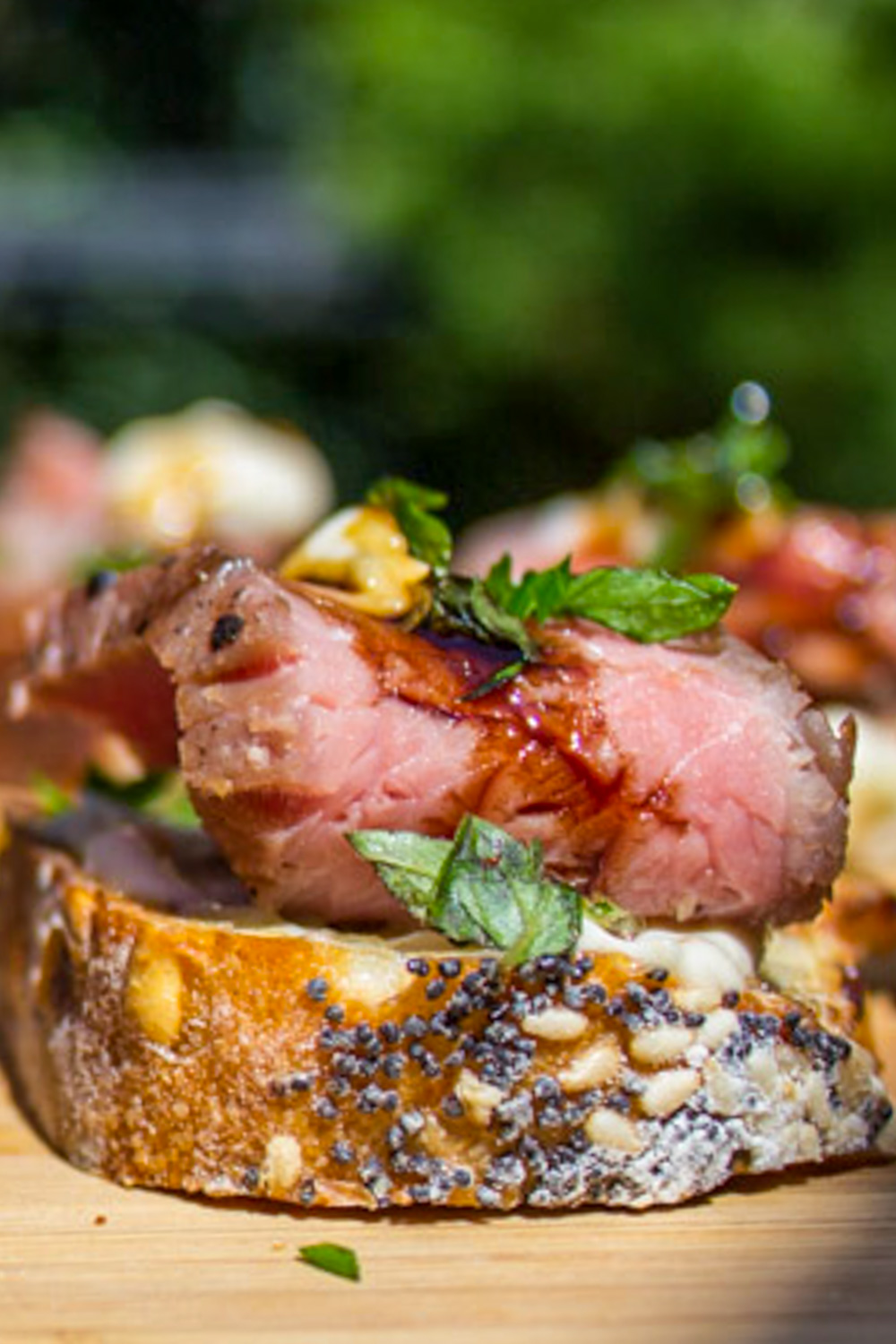 one steak crostini with horseradish aioli sprinkled with parsley on cutting board.