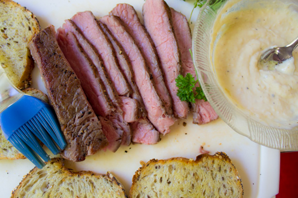 horseradish aioli in bowl, toast slices, sliced steak on cutting board.