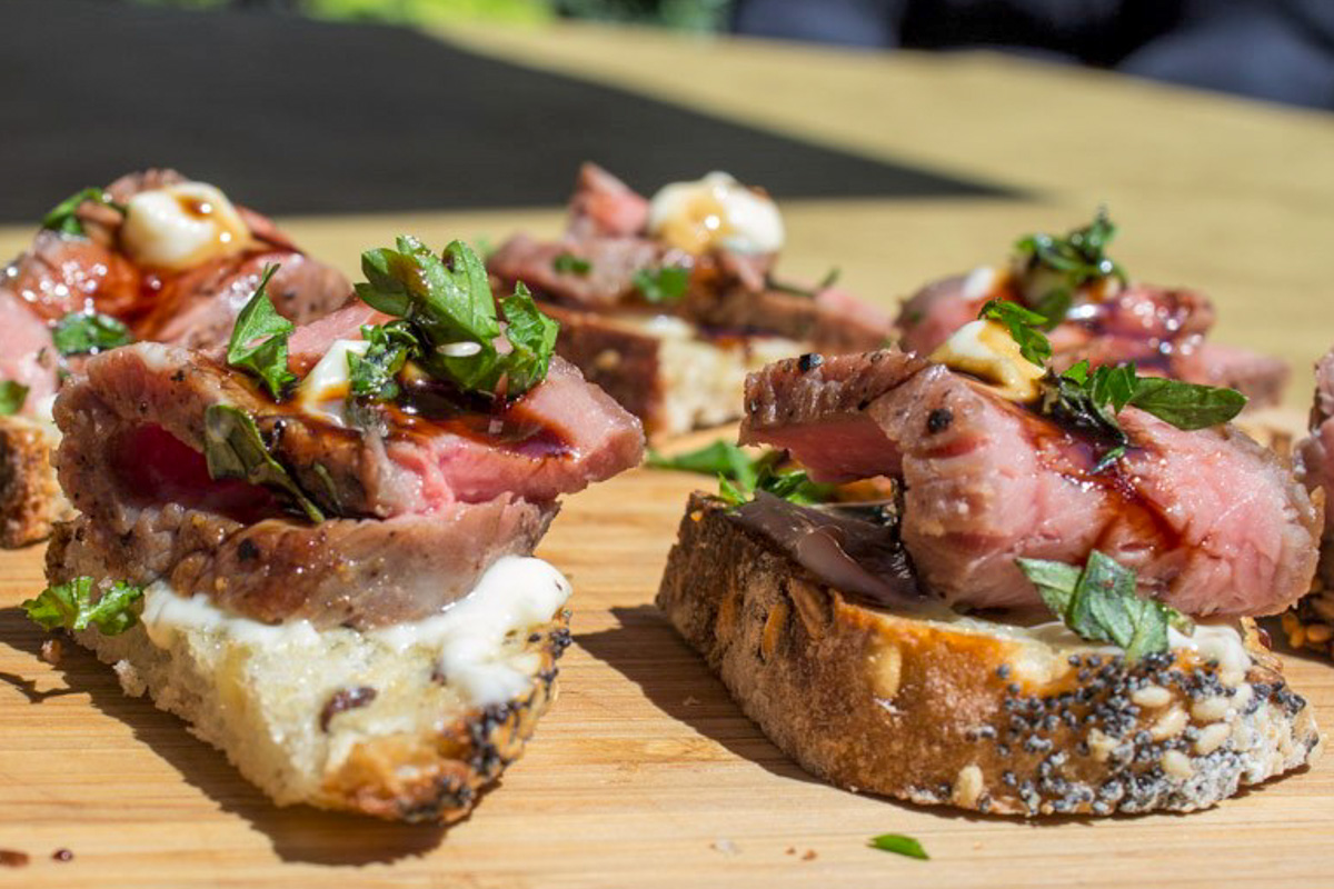 steak crostini pieces with horseradish aioli sprinkled with parsley on cutting board.