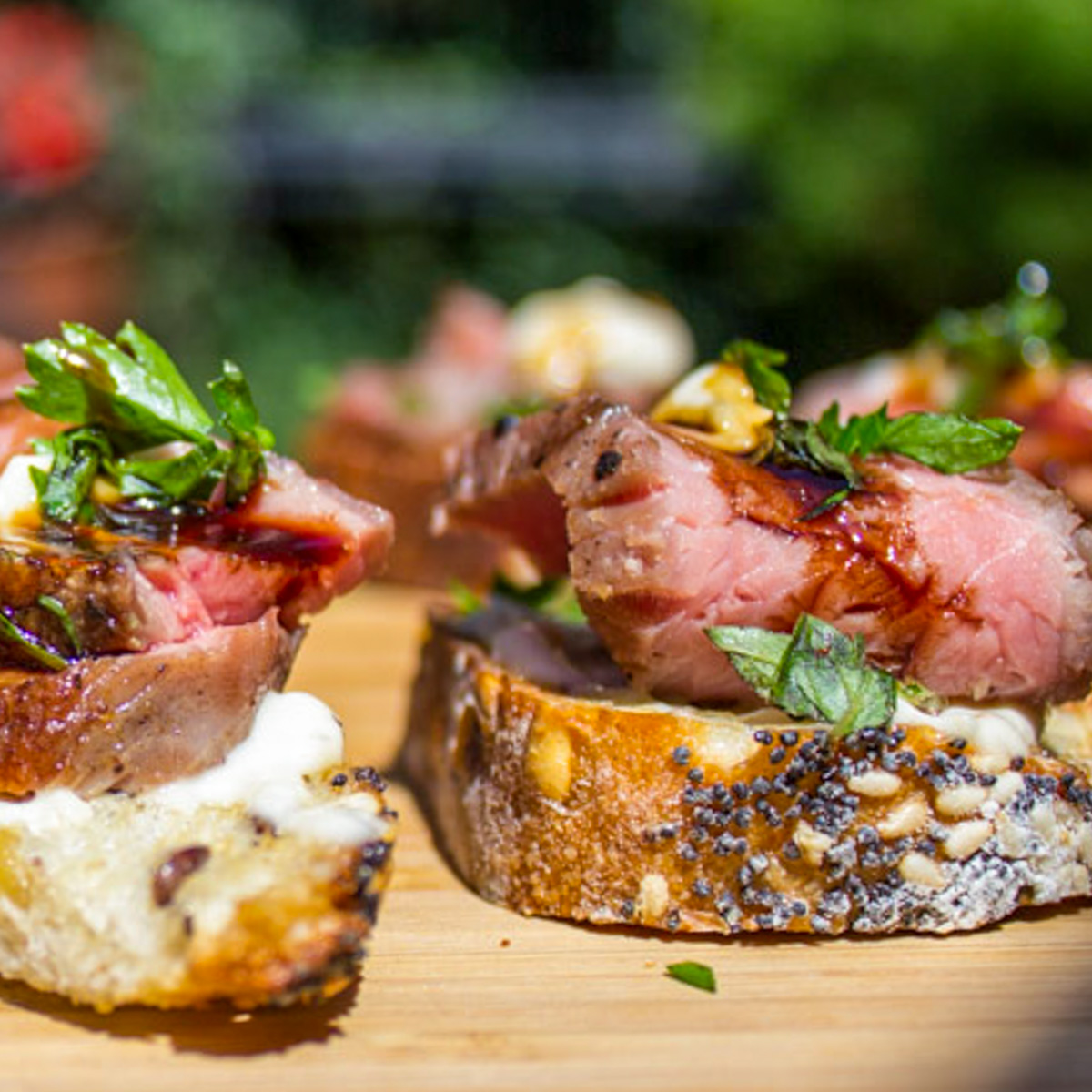steak crostini pieces with horseradish aioli sprinkled with parsley on cutting board.