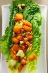 one romaine lettuce leaf with roasted butternut squash salad on white plate.