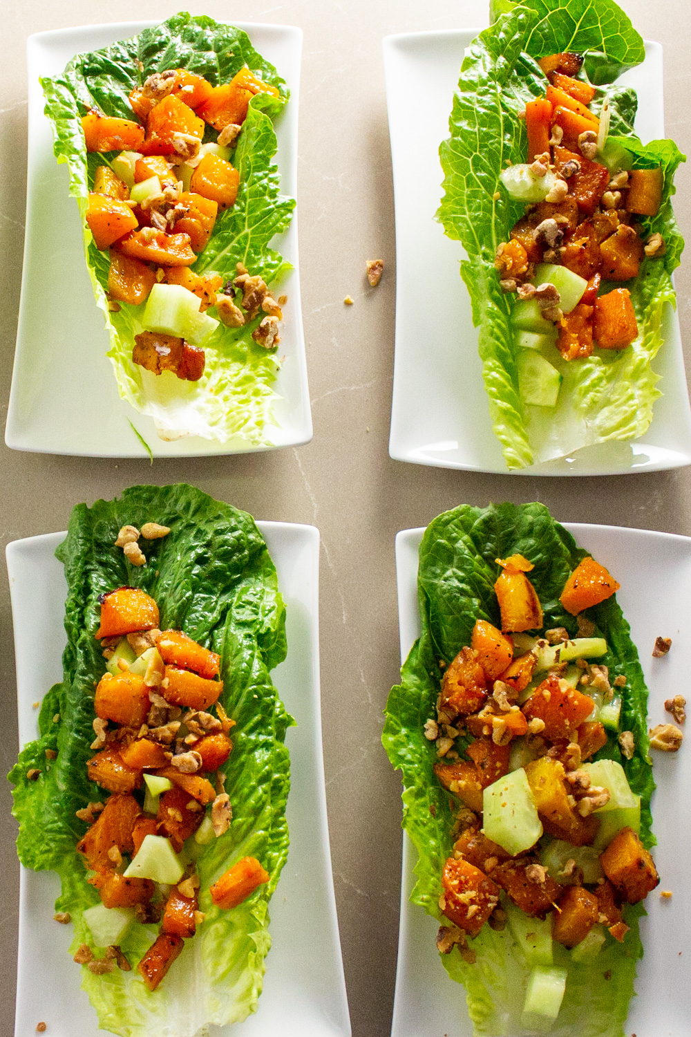 6 plates of romaine lettuce leaves with roasted butternut squash salad on each leaf on white plates.