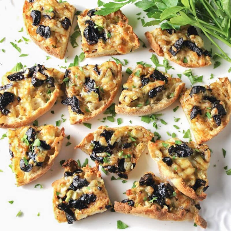 baked olive cheese appetizers on white plate with parsley.
