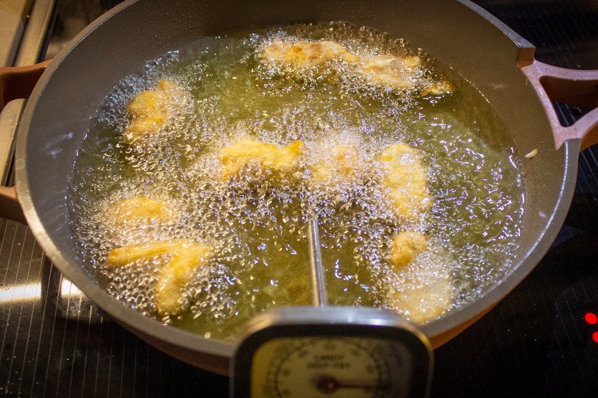 chicken pieces frying in oil in skillet with temperature gauge.