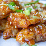 honey garlic chicken pieces on place garnished with sesame seeds and green onion.