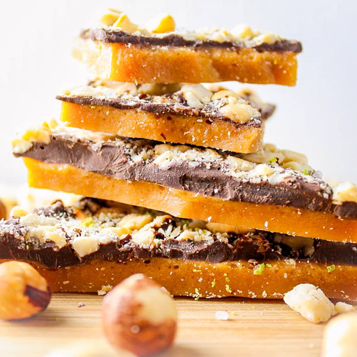 stacked pieces of chocolate covered toffee with hazelnuts on cutting board.
