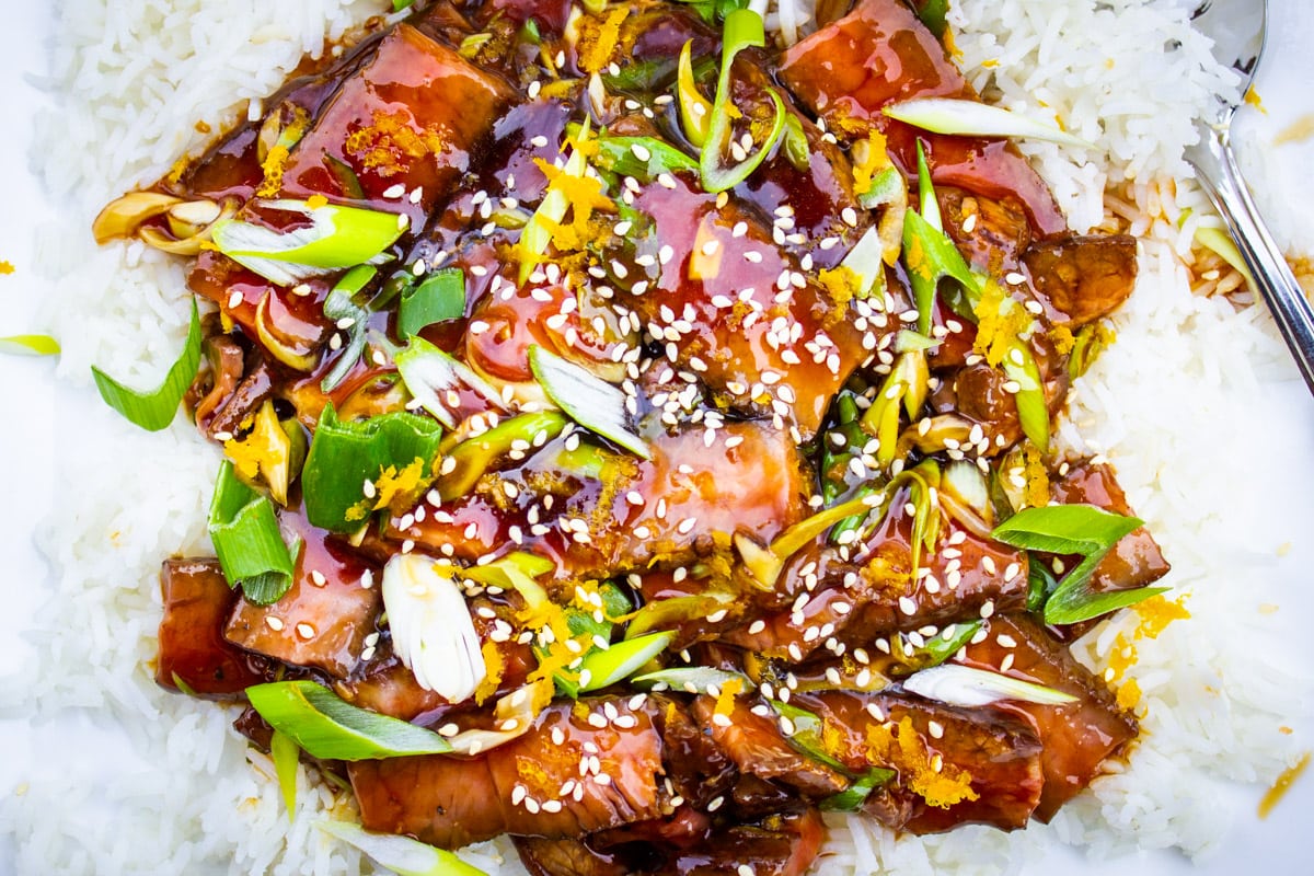 mongolian beef with green onions garnished with sesame seeds over rice in plate.