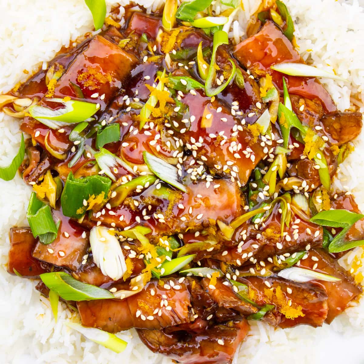mongolian beef with green onions garnished with sesame seeds over rice in plate.