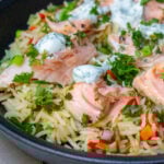 salmon chunks over veggie rice topped with dill sauce and herbs.