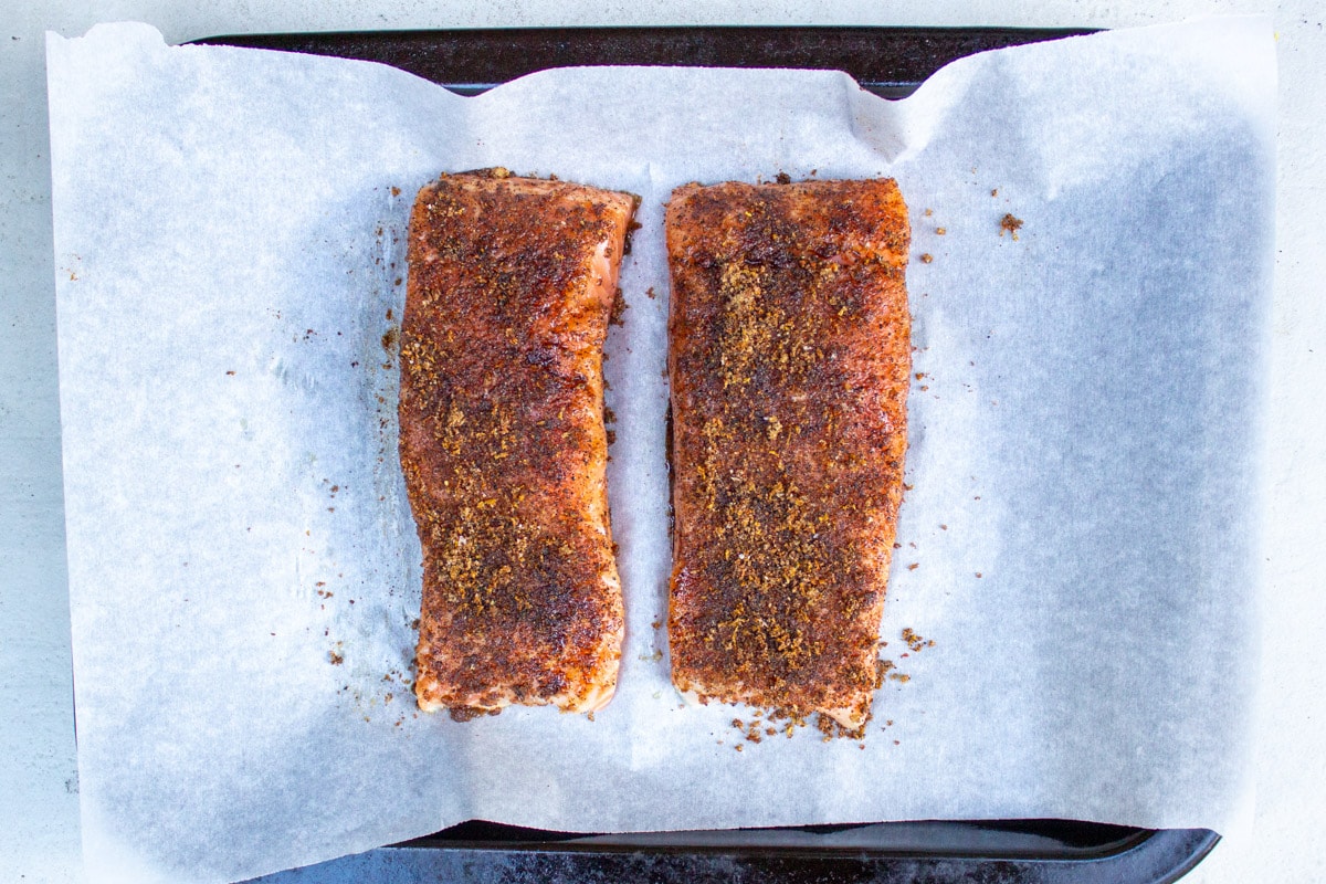 two unbaked seasoned salmon fillets on parchment lined pan.