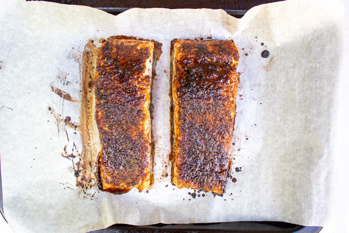 two baked seasoned salmon fillets on parchment lined pan.