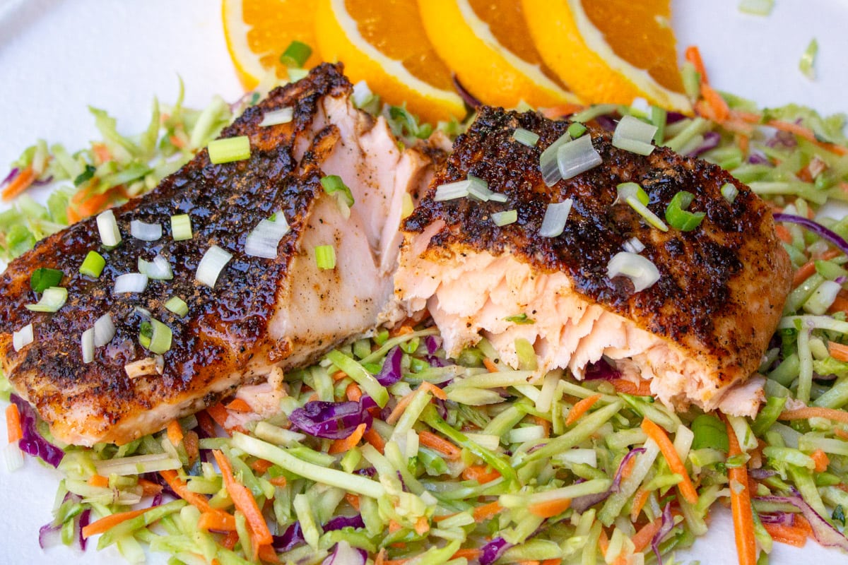 salmon fillet cut in half over coleslaw with orange slices on plate.