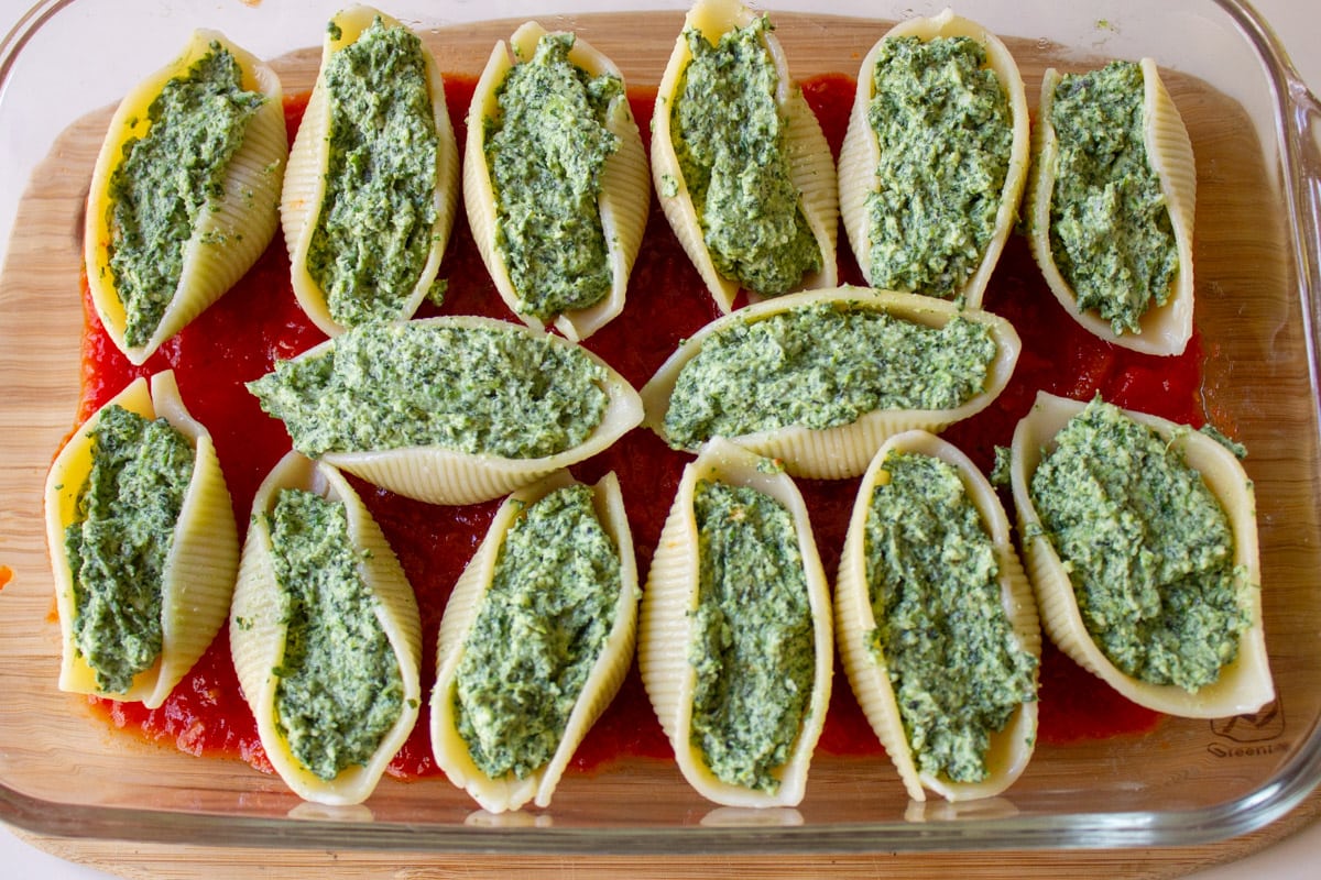 spinach and cheese mixture stuffed into pasta shells sitting on sauce in casserole dish.