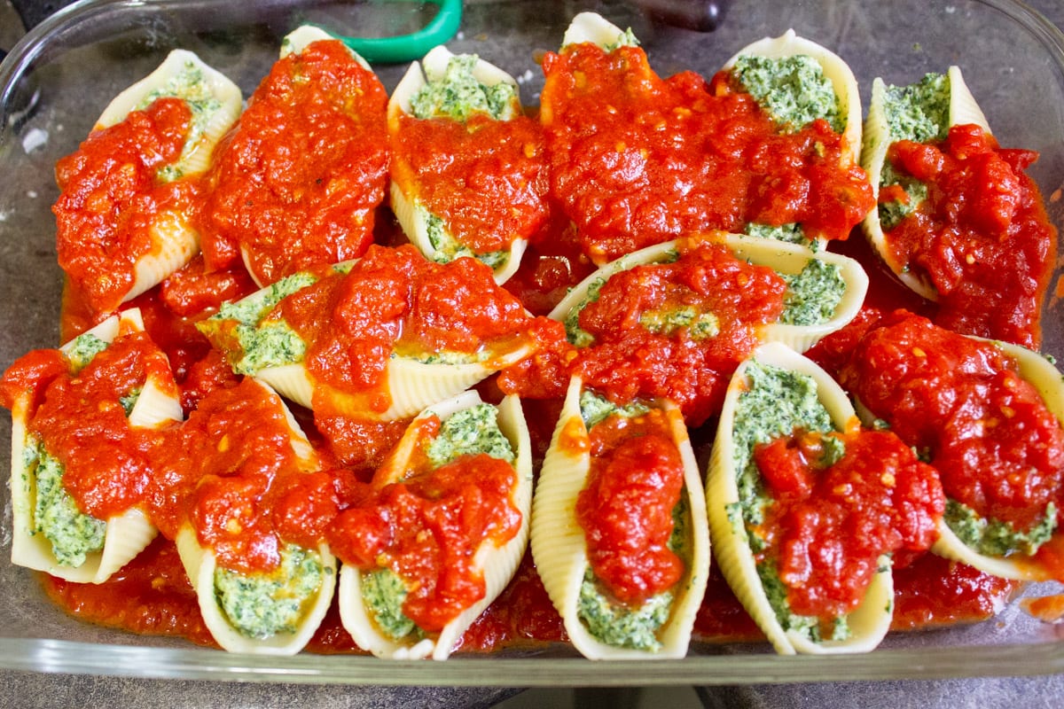 tomato sauce on top of stuffed shells in casserole dish.