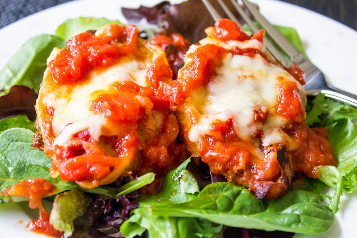 cheese and ricotta stuffed shells toped with tomato sauce served over bed of lettuce on plate.