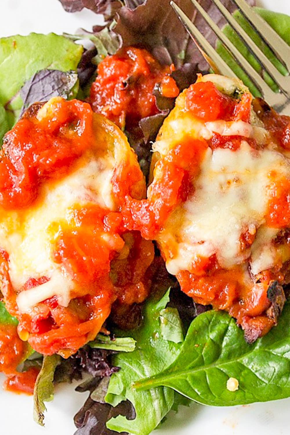 cheese and ricotta stuffed shells toped with tomato sauce served over bed of lettuce on plate.