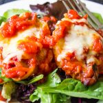 cheese and ricotta stuffed shells toped with tomato sauce served over bed of lettuce on plate.