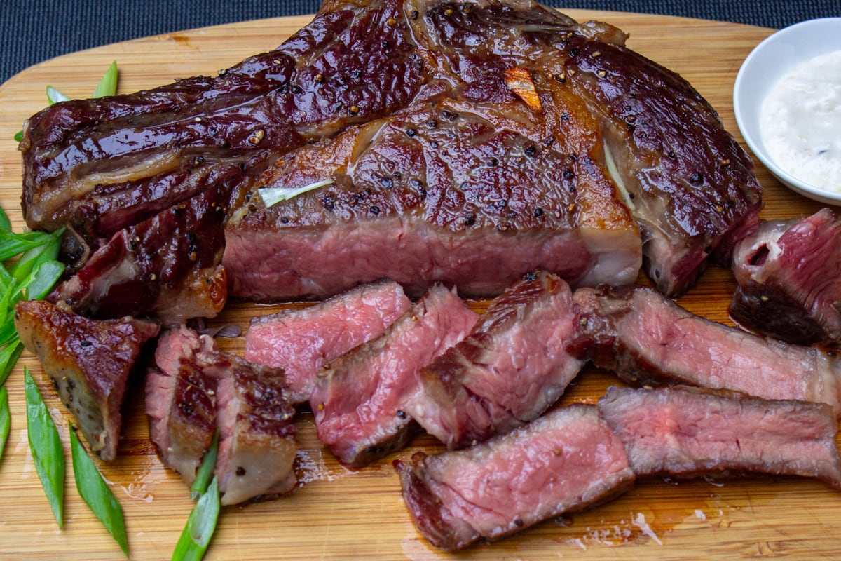 reverse seared ribeye steak partly sliced on cutting board.