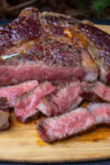 reverse seared ribeye steak partly sliced on cutting board.