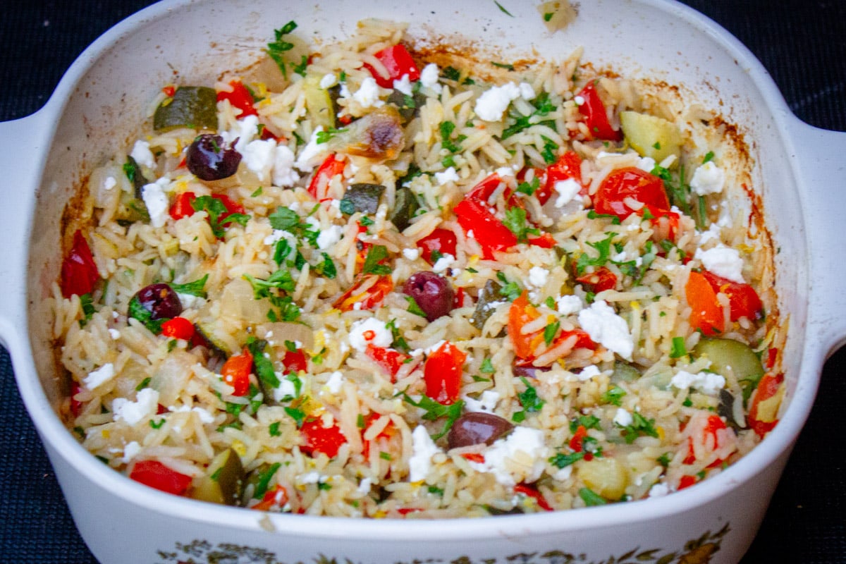 Mediterranean rice with vegetables, feta, olives and lemon in casserole dish.