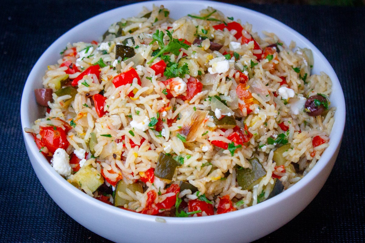 Mediterranean rice with vegetables, feta, olives and lemon in bowl.