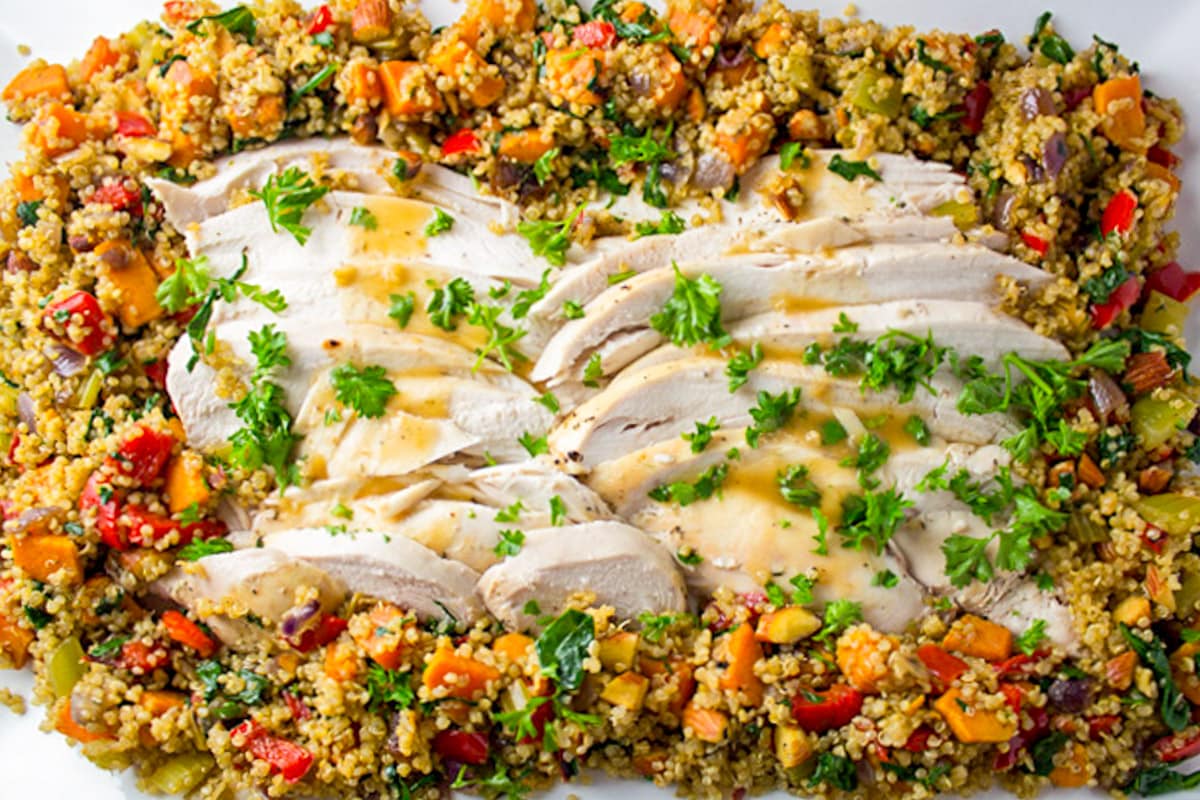 sliced turkey and gravy surrounded by vegetable quinoa stuffing on platter.