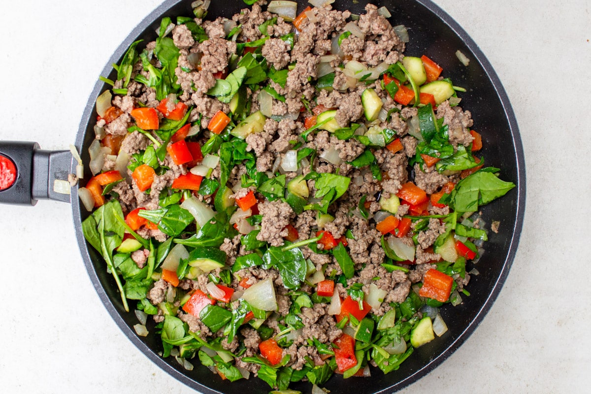 cooked beef and vegetables and spinach in skillet.