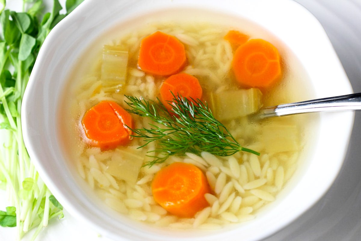 chicken soup with orzo, carrots and dill in bowl.