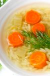 chicken soup with orzo, carrots and dill in bowl.