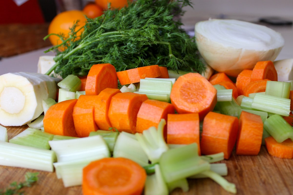 cut up carrots, parsnip, celery, onion and dill on cutting board. 