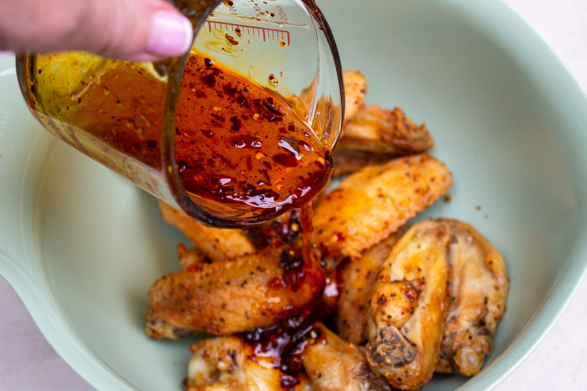 hot honey glaze pouring over baked chicken wings in bowl.