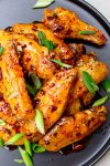 glazed chicken wings on black plate with green onion garnish.
