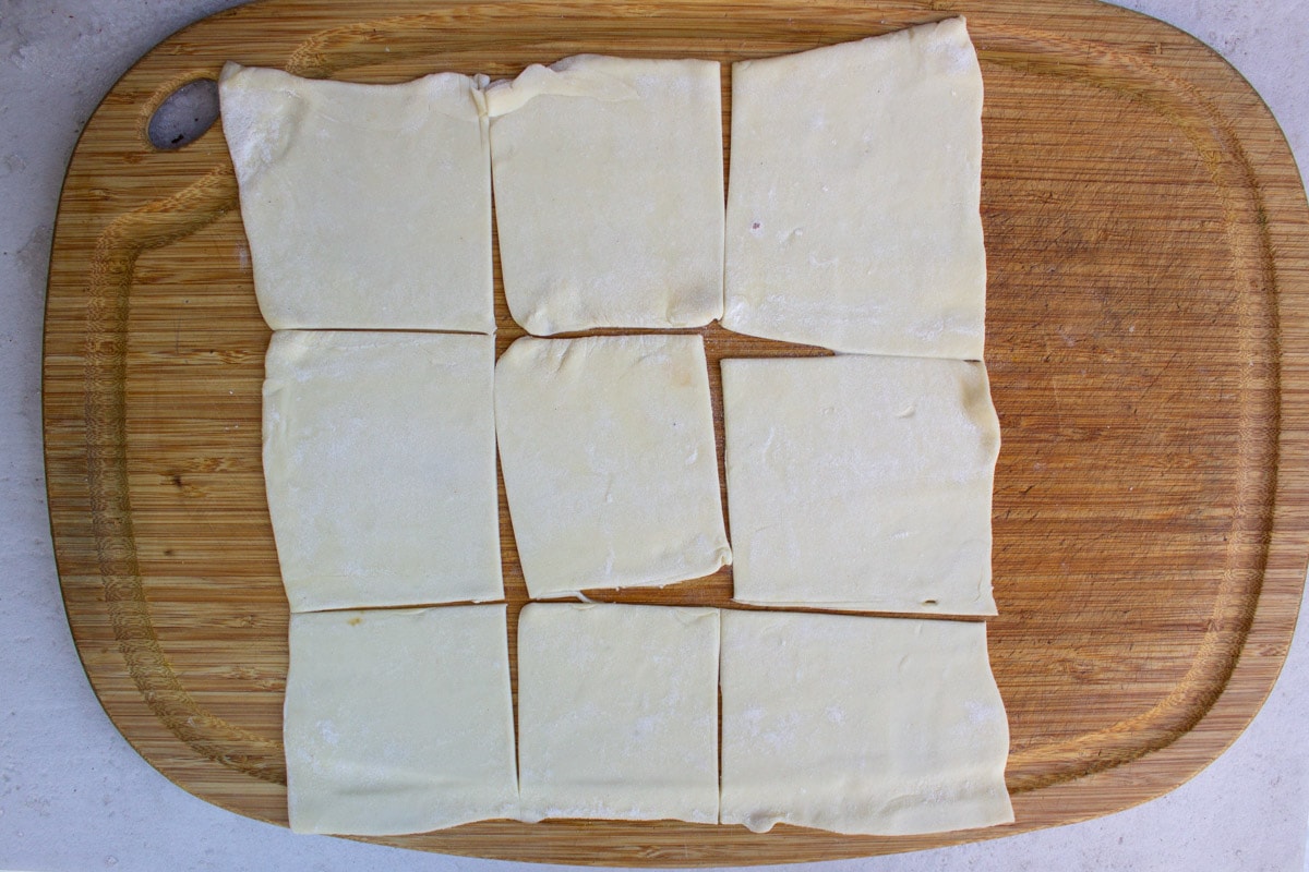 pastry sheet cut into 9 squares on cutting board.