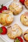 mini apple pies dusted with powdered sugar on plate with strawberries.